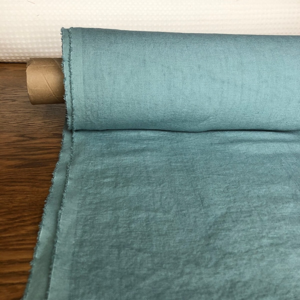 Puede incluir: Un rollo de tela azul turquesa con una superficie ligeramente texturizada. La tela está enrollada y asegurada con un tubo de papel marrón.