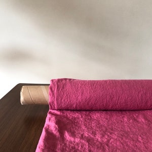 Puede incluir: Un rollo de tela de lino rosa sobre una superficie de madera. La tela está doblada y enrollada, con los extremos metidos.