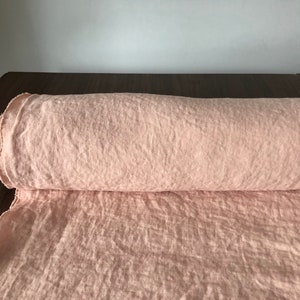 May include: A roll of pale pink linen fabric. The fabric has a textured, slightly wrinkled appearance.
