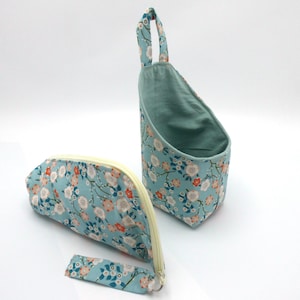 Peut inclure: Deux organisateurs en tissu avec un motif floral sur fond bleu clair. L'un est un panier suspendu avec une poignée, l'autre une pochette zippée. Le motif floral comprend des fleurs blanches, oranges et bleues.