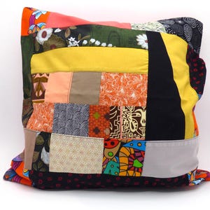 Peut inclure: Coussin carré en patchwork avec une variété de motifs et de couleurs de tissus. Le coussin présente un mélange de motifs floraux, géométriques et abstraits dans des tons orange, jaune, noir et vert. Le coussin mesure environ 46 cm de côté.