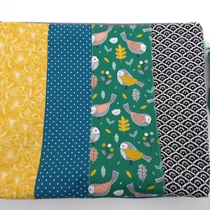 Peut inclure: Une pochette rectangulaire avec une fermeture éclair et une dragonne. La pochette est divisée en cinq panneaux verticaux avec différents motifs : floral jaune, pois bleu canard, oiseaux et feuilles verts, et motifs géométriques noirs et blancs.