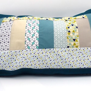 Peut inclure: Un coussin rectangulaire décoratif avec un motif patchwork. Le coussin a une bordure turquoise et un panneau central avec diverses bandes de tissu à motifs en turquoise, beige et blanc. Les motifs comprennent des formes géométriques et des motifs floraux.