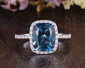 May include: A silver ring with a cushion-cut blue topaz gemstone surrounded by a halo of smaller diamonds. The ring has a pave setting with smaller diamonds on the band.