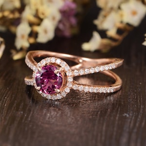 Op de afbeelding: Een verlovingsring van roségoud met een ronde roze edelsteen omgeven door een halo van kleinere diamanten. De ring heeft een gesplitste band met een rij diamanten aan elke kant.