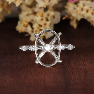 May include: A silver ring setting with an oval-shaped center stone and small round stones on the band.