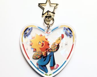 Può includere: Un portachiavi in ​​acrilico trasparente a forma di cuore con un ciondolo a stella dorata. Il portachiavi presenta un personaggio dei cartoni animati con una testa gialla a forma di sole, pantaloni blu e una camicia con motivi colorati. Il personaggio tiene un fiore rosso e ha un'espressione sorpresa.
