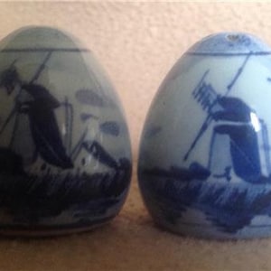 May include: Two blue and white ceramic salt and pepper shakers shaped like eggs. Each shaker features a traditional Dutch windmill design.