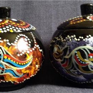May include: Two black ceramic round jars with lids, decorated with colourful abstract patterns and white dots. The jars are painted with a variety of colours, including red, blue, yellow, green, and purple.