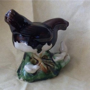May include: A ceramic figurine of a brown and white hen with a green and brown base. The hen is surrounded by three smaller white chicks.