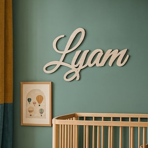Peut inclure: Intérieur de chambre d'enfant avec un lit bébé en bois, une image encadrée de montgolfières et une enseigne en bois avec le nom "Lyam". La pièce a un mur vert, un tapis rayé et un jouet dinosaure vert.