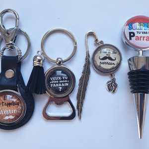 Peut inclure: Ensemble de cinq porte-clés et bouchons de bouteille fantaisie sur le thème du parrain. Les porte-clés présentent un design noir et blanc avec le texte "Je t'appelais Parrain?" et "Veux-tu etre mon Parrain?" Les bouchons de bouteille présentent un design noir et blanc avec le texte "Veu tu etre mon parrain?" et "Surprise, tu vas etre Parrain".