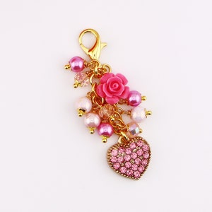 May include: A gold charm with a pink heart, pink flowers, and pink and white beads. The charm is attached to a gold chain.