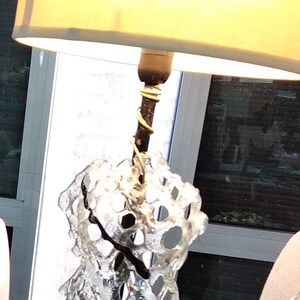 May include: A white glass lamp with a black base and a white fabric lampshade. The glass is shaped like a spiral with holes throughout. The lamp is sitting on a gold sequined table cloth.