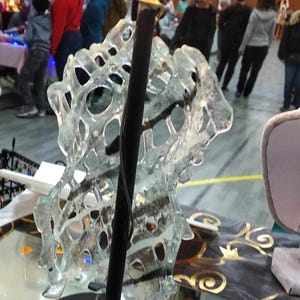 May include: A black table lamp with a clear glass shade. The shade is shaped like a spiral and has a delicate, intricate design. The lamp is sitting on a black surface.