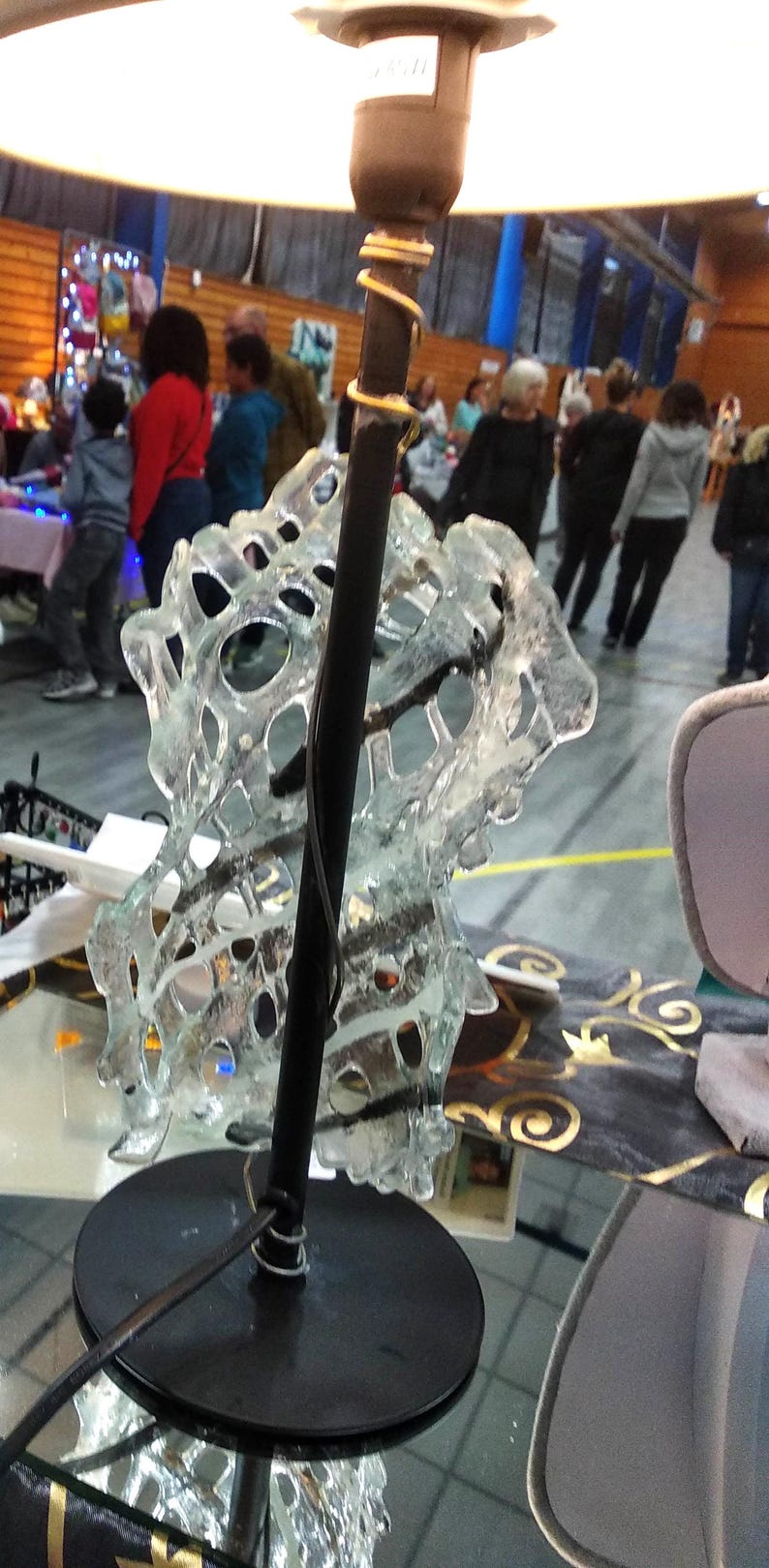 May include: A black table lamp with a clear glass shade. The shade is shaped like a spiral and has a delicate, intricate design. The lamp is sitting on a black surface.
