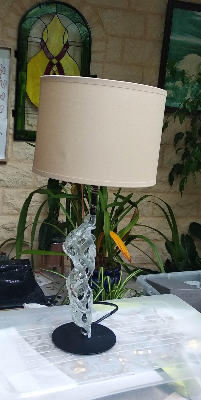 May include: A white lampshade with a glass base shaped like a tree branch. The lamp is on a white surface.