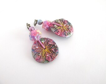 Könnte beinhalten: Handgefertigte Ohrringe mit floralem Design. Die runden Anhänger zeigen ein erhabenes Blumenmuster in Rosa, Gelb und Grün. Kleine Perlen und ein Perlenstiel ergänzen das Design. Die Ohrringe sind vor weißem Hintergrund abgebildet.