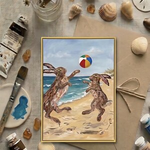 Peut inclure: Une peinture rectangulaire encadrée représentant deux lièvres bruns jouant avec un ballon de plage coloré sur une plage de sable près de l'océan. L'œuvre présente des coups de pinceau visibles et un ciel bleu clair, dans un cadre doré.