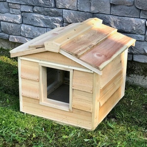 May include: A wooden dog house with a sloped roof and a rectangular entrance. The house is made of natural wood and has a light brown color.