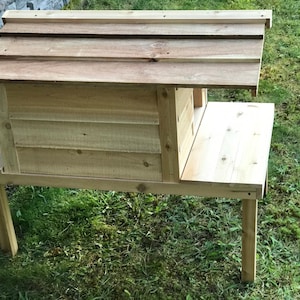 May include: A wooden birdhouse with a raised platform and a slanted roof. The birdhouse is made of natural wood and is elevated on four legs.
