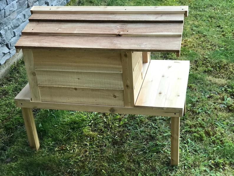 May include: A wooden birdhouse with a raised platform and a slanted roof. The birdhouse is made of natural wood and is elevated on four legs.