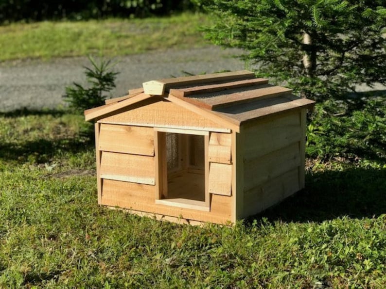 May include: A wooden dog house with a cedar shingle roof. The house has a small window and a raised platform for the dog to enter.