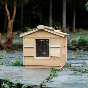 May include: A wooden cat house with a small window and a shingled roof. The house is made of natural wood and has a rustic look.