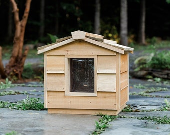May include: A wooden cat house with a small window and a shingled roof. The house is made of natural wood and has a rustic look.
