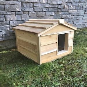 May include: A wooden dog house with a slanted roof and a single entrance. The house is made of natural wood and has a rustic appearance.