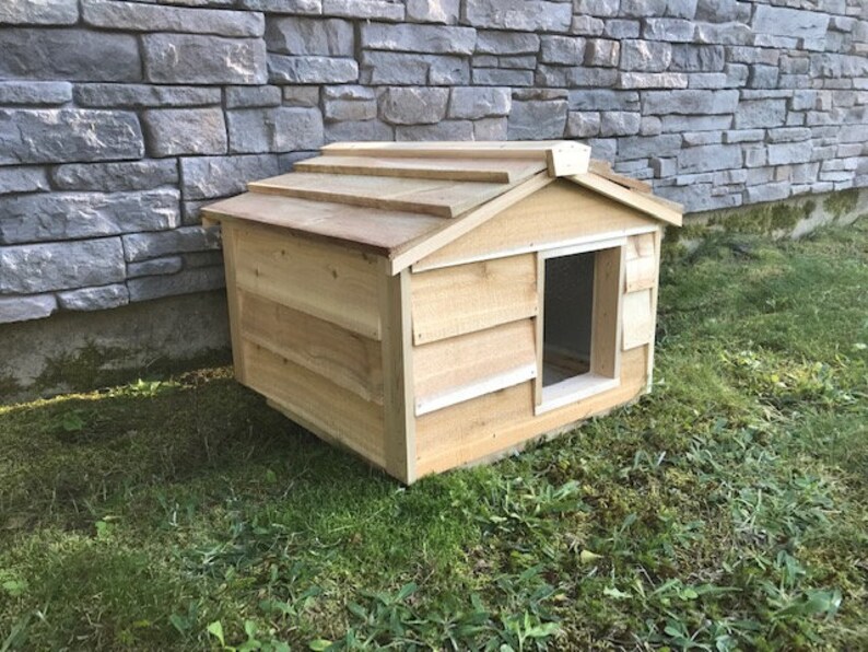 May include: A wooden dog house with a slanted roof and a single entrance. The house is made of natural wood and has a rustic appearance.