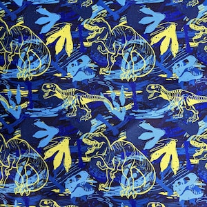 Könnte beinhalten: Blauer Stoff mit einem sich wiederholenden Muster aus gelben und blauen Dinosauriern, Dinosaurierskeletten und Dinosaurierspuren. Der Hintergrund ist dunkelblau mit blauen und gelben Farbspritzern.