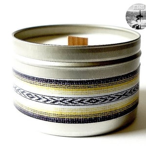 May include: A silver candle tin with a white candle inside. The tin has a black, white, and yellow patterned band around the middle. The lid is off and a wooden wick is visible.