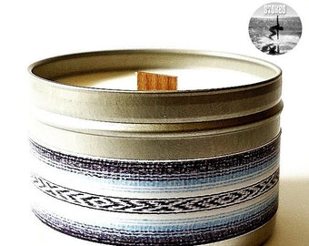 May include: A silver candle tin with a white candle and a wooden wick. The tin has a blue, white, and black striped pattern.