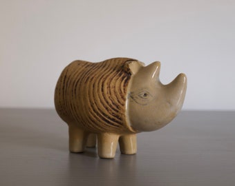 Może przedstawiać: Ceramiczna figurka nosorożca w brązowe i beżowe paski z jasnobrązową twarzą. Figurka ma stylizowane oko i mały róg.