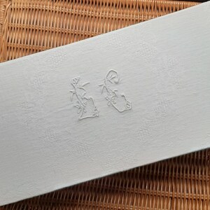 May include: White linen table runner with embroidered floral designs. The embroidery features two stylized floral motifs, each with a central flower and leaves.