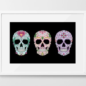 May include: A framed print showing three pixelated sugar skulls. Each skull is decorated with floral and heart designs in pastel colours, set against a black background.