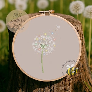 May include: A cross-stitch embroidery of a dandelion with colourful accents, set in a wooden hoop. The design is on a light beige fabric, with the text "PDF Pattern Digital download" and "Crazy Bee Patt" visible.