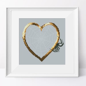 May include: A gold heart-shaped frame with a spider web inside. The web is white and the frame is a dark gold color. There are three black spiders on the web.