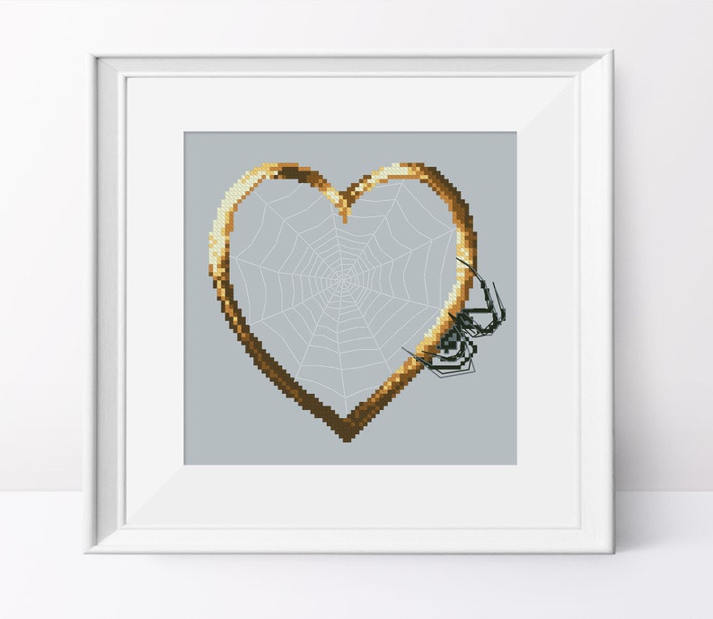 May include: A gold heart-shaped frame with a spider web inside. The web is white and the frame is a dark gold color. There are three black spiders on the web.
