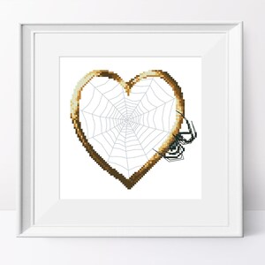 May include: A brown heart-shaped frame with a spider web inside. A black spider is sitting on the web.