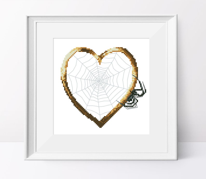 May include: A brown heart-shaped frame with a spider web inside. A black spider is sitting on the web.