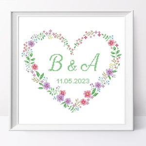 Puede incluir: Un marco blanco con un corazón verde hecho de flores y hojas. El corazón tiene las iniciales "B & A" y la fecha "11.05.2023" en su interior.