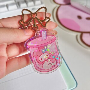 Puede incluir: Charm de llavero de pl&aacute;stico rosa y transparente con forma de vaso de boba con un personaje de dibujos animados rosa en su interior. El charm tiene purpurina y estrellas en su interior.