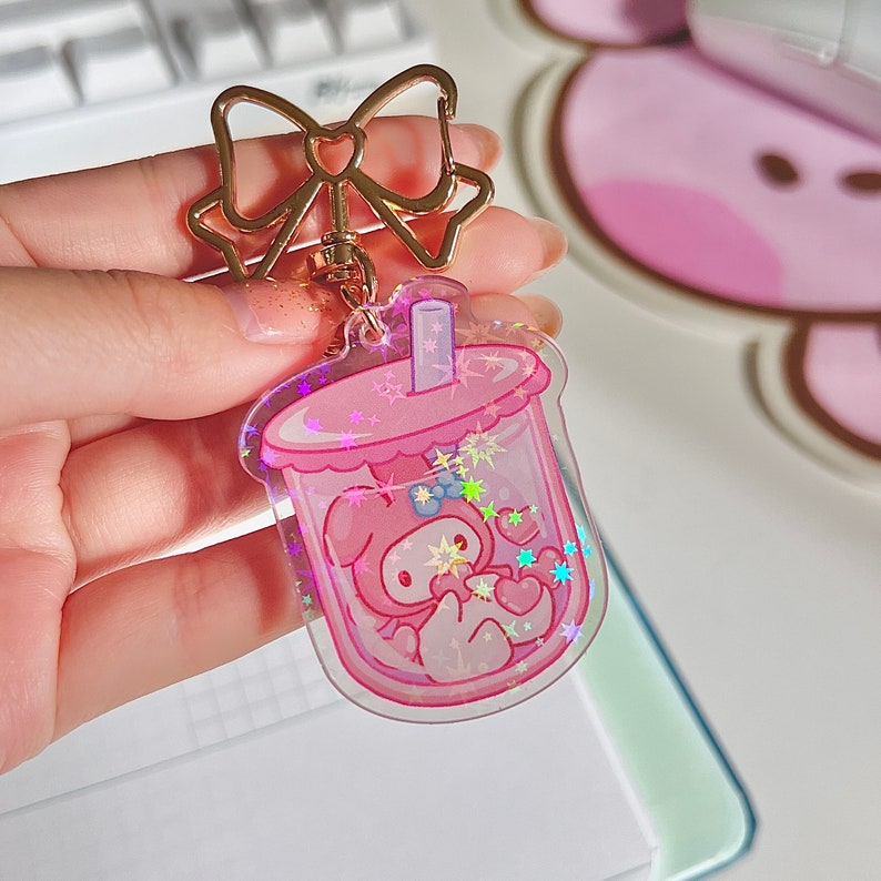 Puede incluir: Charm de llavero de pl&aacute;stico rosa y transparente con forma de vaso de boba con un personaje de dibujos animados rosa en su interior. El charm tiene purpurina y estrellas en su interior.