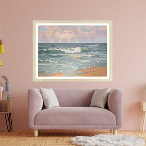 May include: Framed artwork depicting a coastal scene with ocean waves, seagulls, and a sandy beach. The painting features a light-colored wooden frame and is displayed above a pink sofa. The artwork captures a serene beach landscape.