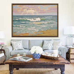 May include: A living room scene featuring a framed seascape painting above a gray sofa with decorative pillows. A dark wood coffee table holds a blue and white vase with white flowers. Two wicker chairs and a side table with a lamp complete the decor.