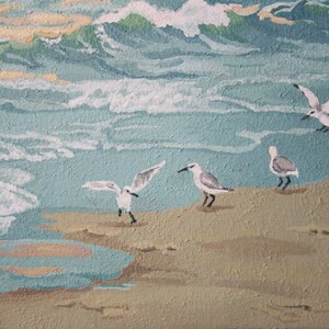 May include: An acrylic painting of a beach scene with seagulls. The artwork depicts waves in shades of blue and green, with seagulls on the sand. The painting has a textured appearance, with the artist's signature in the bottom right corner.