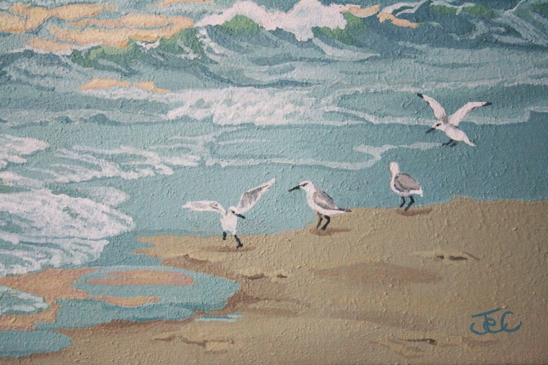 May include: An acrylic painting of a beach scene with seagulls. The artwork depicts waves in shades of blue and green, with seagulls on the sand. The painting has a textured appearance, with the artist's signature in the bottom right corner.