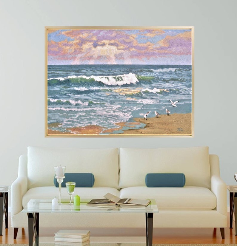 May include: A framed artwork depicting a coastal scene. The painting showcases ocean waves in shades of blue and green, crashing onto a sandy beach. Several seagulls are on the shore. The sky features a blend of pink, purple, and blue hues, suggesting a sunrise or sunset.
